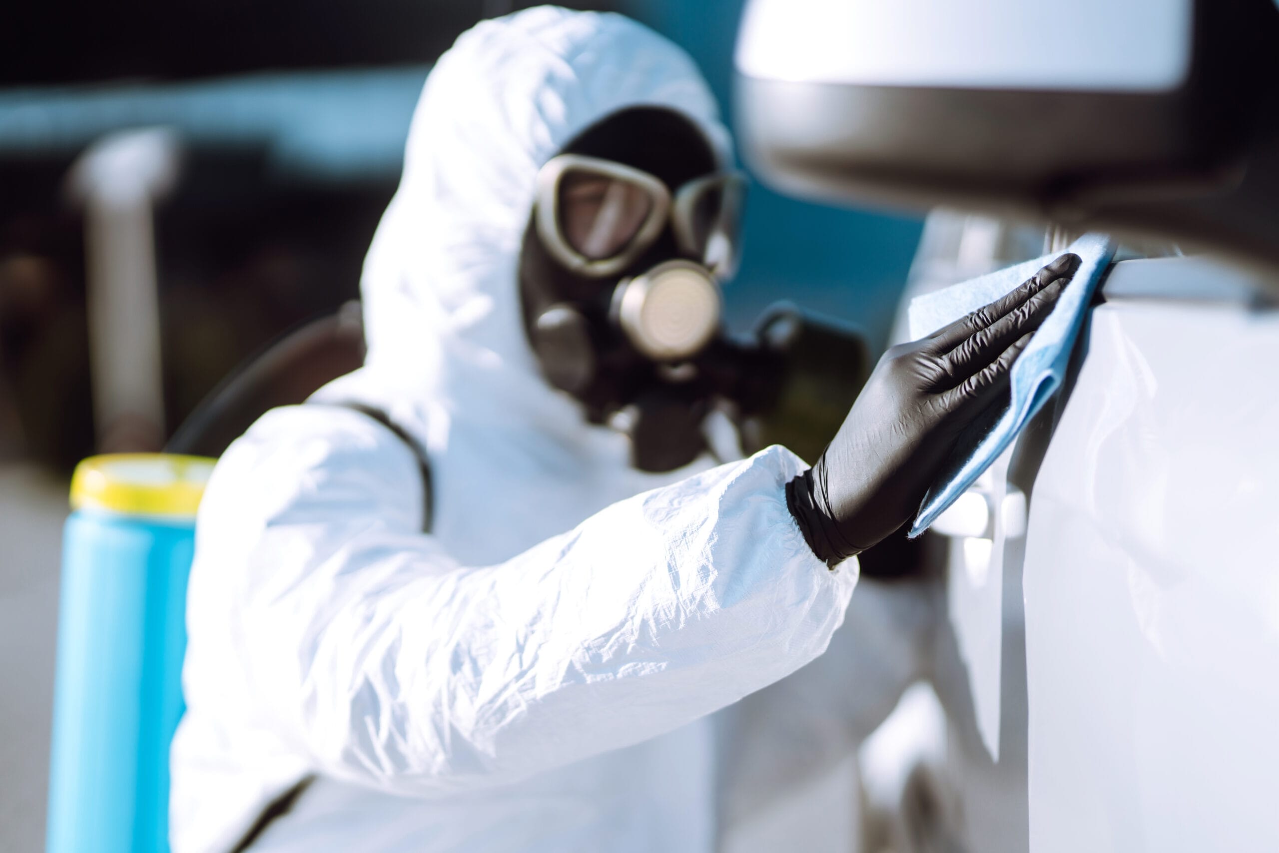 Person in protective suit disinfecting car handles during tear gas cleanup Dallas, highlighting pandemic precautions.