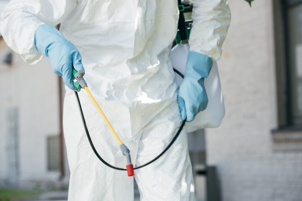 Pest control worker in protective gear holding a sprayer, focusing on the equipment and safety attire for effective pest mana