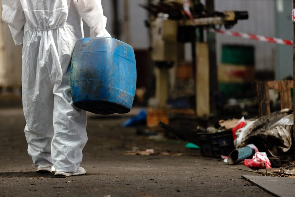 Female worker in hazmat suit holding a chemistry tank in an industrial setting, focusing on safety and inspection.