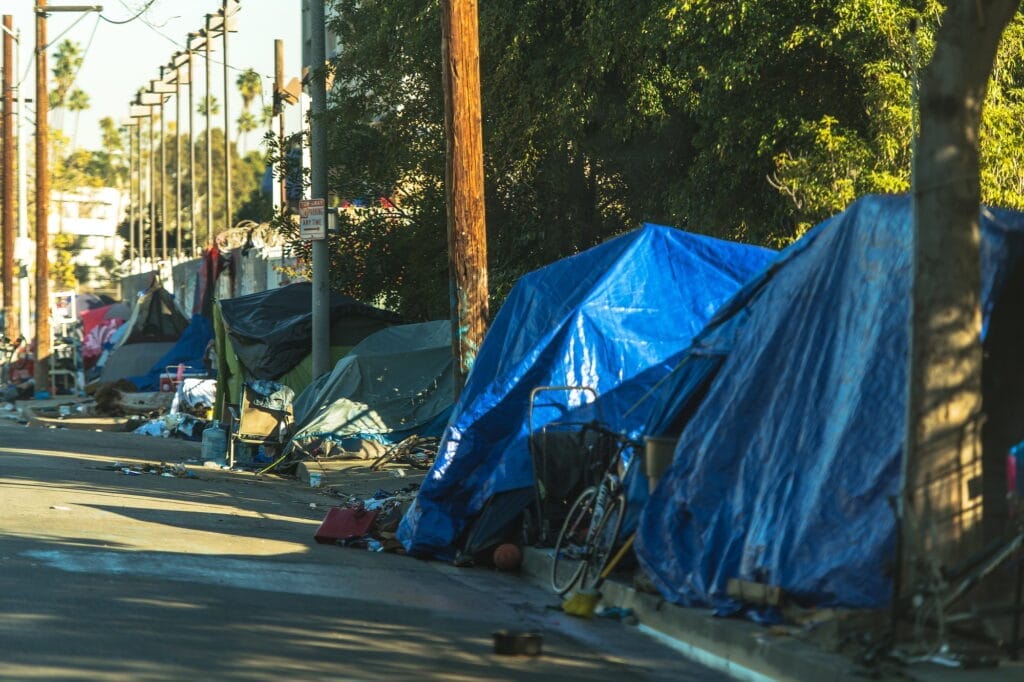 A street in West Hollywood lined with colorful tents and makeshift shelters, highlighting the homelessness issue.