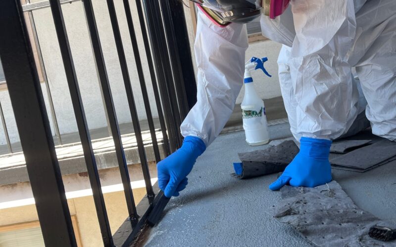 Worker using a power scrubber to clean a concrete surface outdoors, surrounded by industrial equipment and safety barriers.