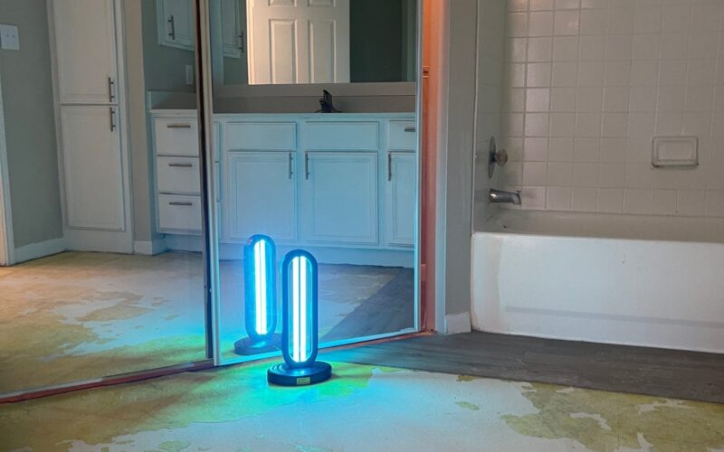 UV-C disinfectant lamp with a sleek design, emitting blue light, placed on a table in a dimly lit room.
